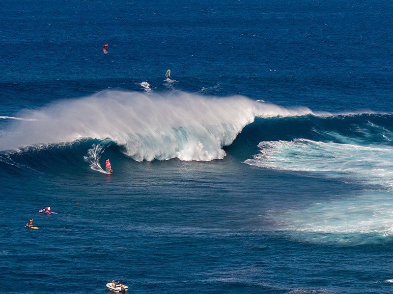Surfers riding massive waves on Maui’s North Shore, a hotspot for world-class surfing near coastal homes